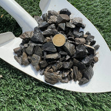 Load image into Gallery viewer, A shovel full of dark charcoal grey 25mm roundle rock, with a coin used for scale in the center.