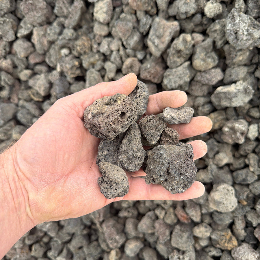Hand holding a small pile of dark rocks against a background of similar rocks